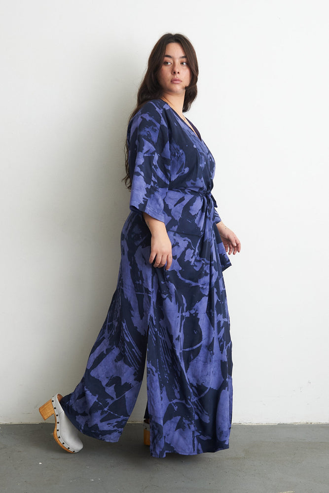 Blueish purple Letsa dress with abstract brush stroke pattern, tied waist, and white ankle-wrap sandals.