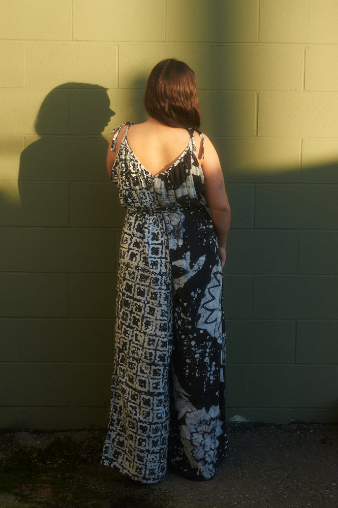 Back view of the Ligo Jumpsuit in 2 Party System print, with intricate black and white designs, against green wall.