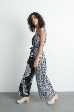 Side view of model in Ligo Jumpsuit with contrasting patterns, sleeveless design, and tie waist, against a plain backdrop.