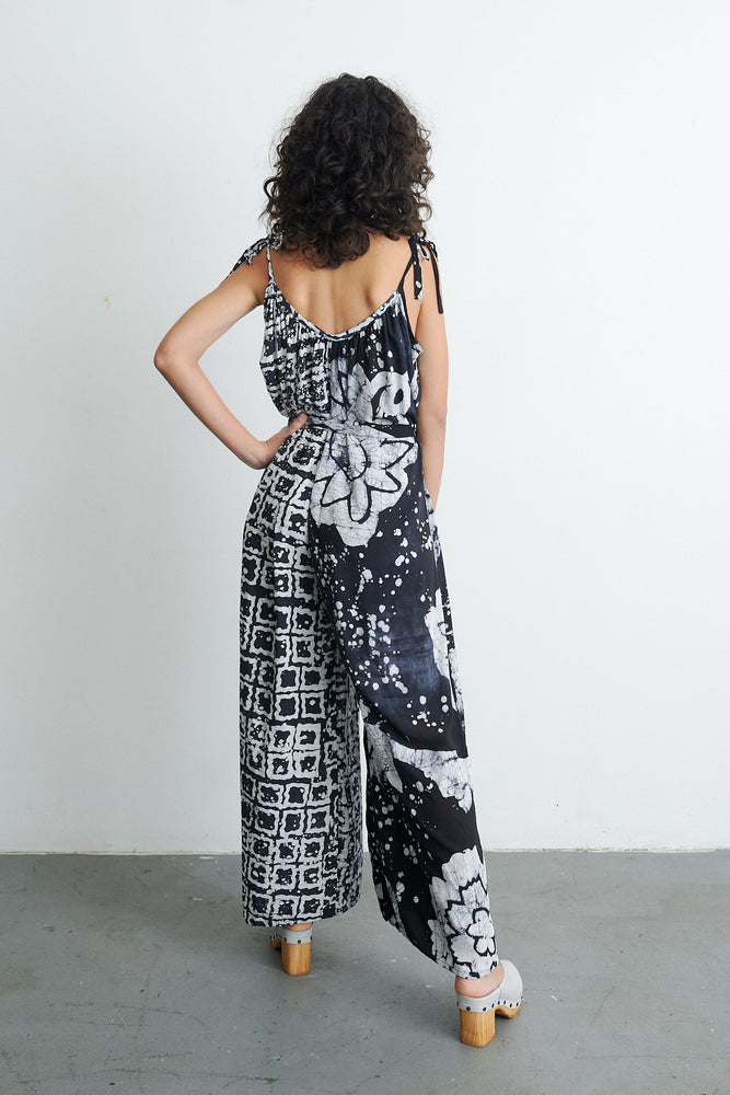 Back view of the sleeveless Ligo Jumpsuit in 2 Party System print, with black and white designs, against a white wall.