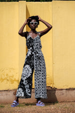 Flowy Ligo Jumpsuit in black and white 2 Party System print with tie straps and sash, against yellow wall.
