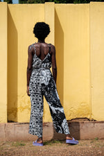 Back view of the Ligo Jumpsuit in abstract black and white pattern, with adjustable tie straps, against a yellow wall.