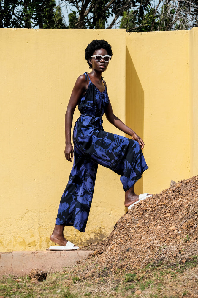 Chic Ligo Jumpsuit in Rorschach print, featuring a loose fit and tie sash, against a bright yellow wall on a clear day.