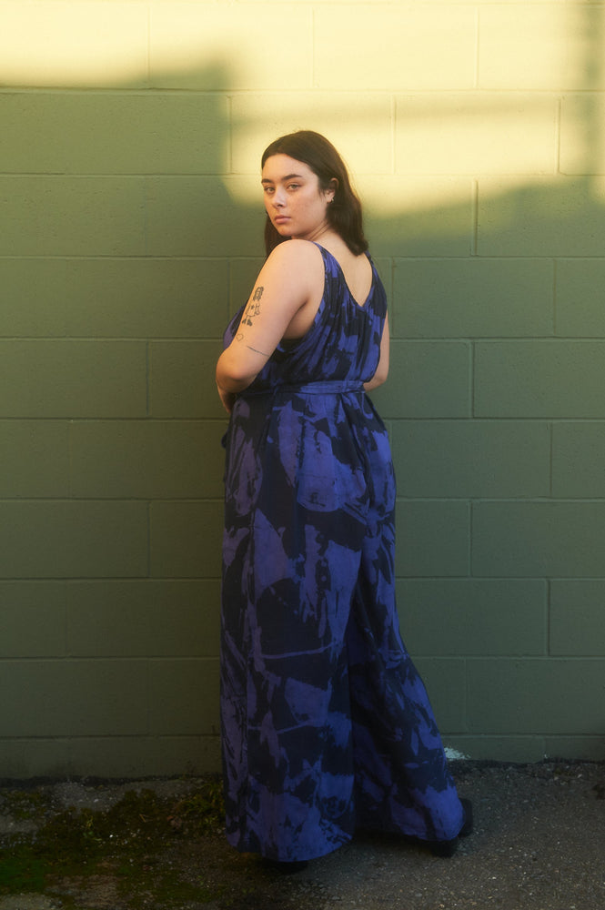 Side view of the Ligo Jumpsuit in Rorschach print, model poses against a green wall, giving an airy, flowy feel.