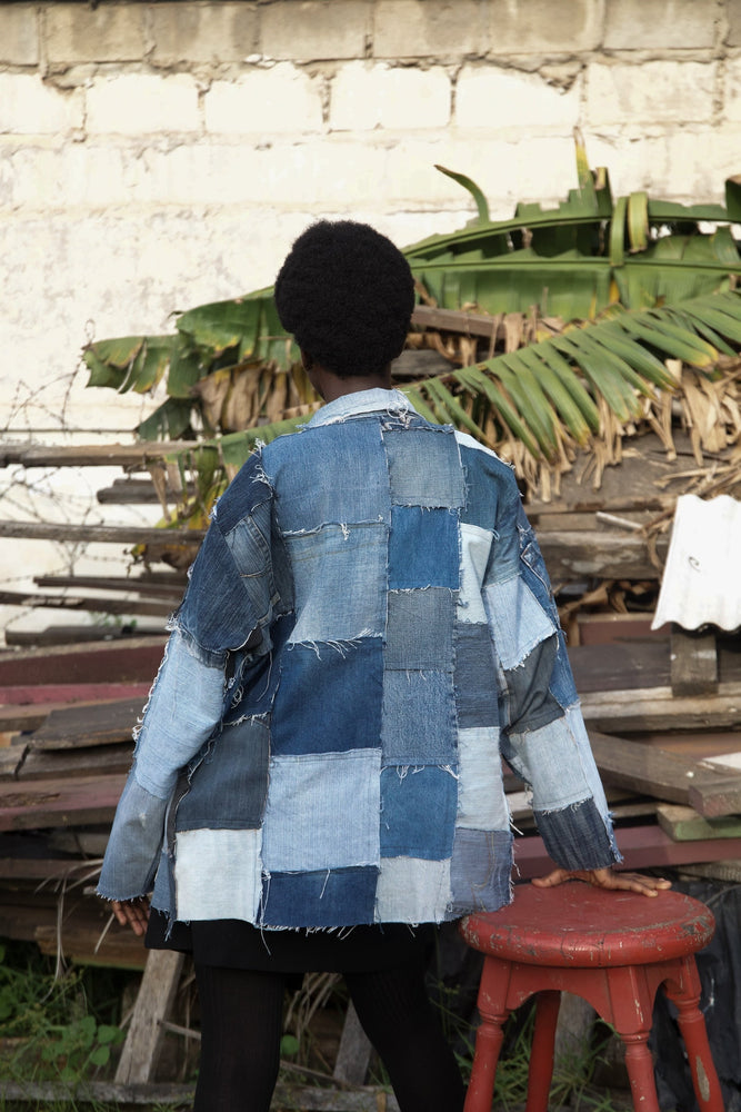 Back view of a woman wearing size 1 of the same denim patchwork jacket casually posing outdoors in front of a pile of wood.
