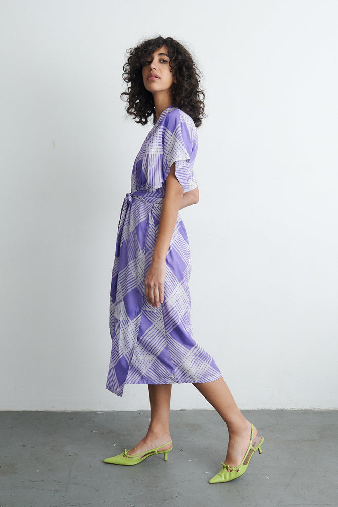 Model in motion wearing the Sampa Dress, with a chunky necklace, against a plain background, highlighting the outfit’s flow.