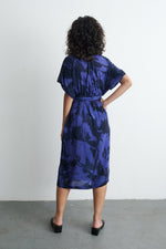 Back view of Sampa Dress with abstract blue pattern, cinched waist, short sleeves, paired with black heels.