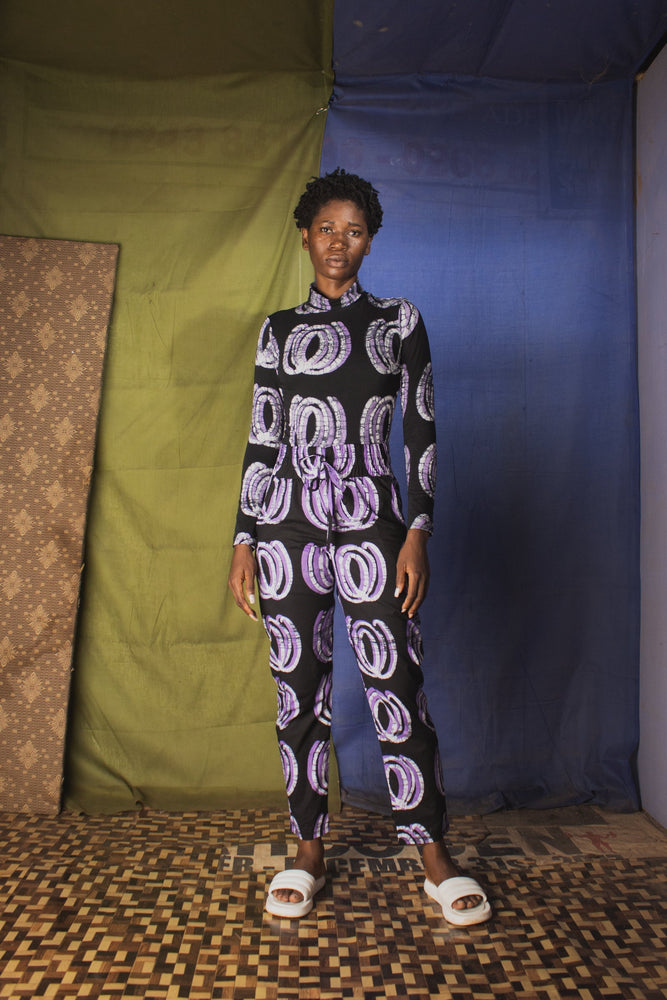 Model in the Stricta Turtleneck in Good Signal a unique print, standing against a backdrop of colorful fabrics.