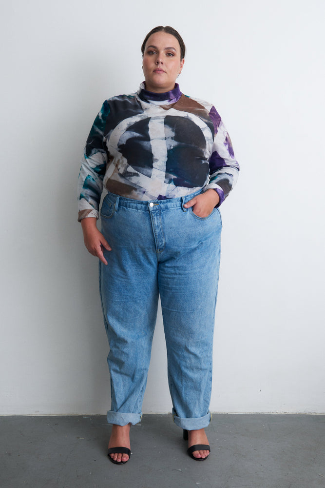 Person in a hand-dye batik shirt with blue, black, and purple hues, paired with high-waisted jeans, against a light backdrop.