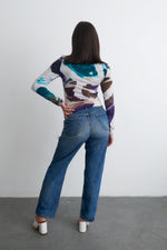 Person in Osei-Duro abstract patterned top and jeans, showcasing the vibrant hand-dyed print, ideal for casual wear.