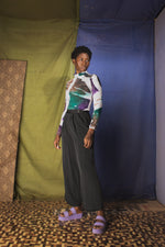 Person in Osei-Duro galaxy print shirt and dark pants, with purple sandals, against a fabric-draped backdrop.