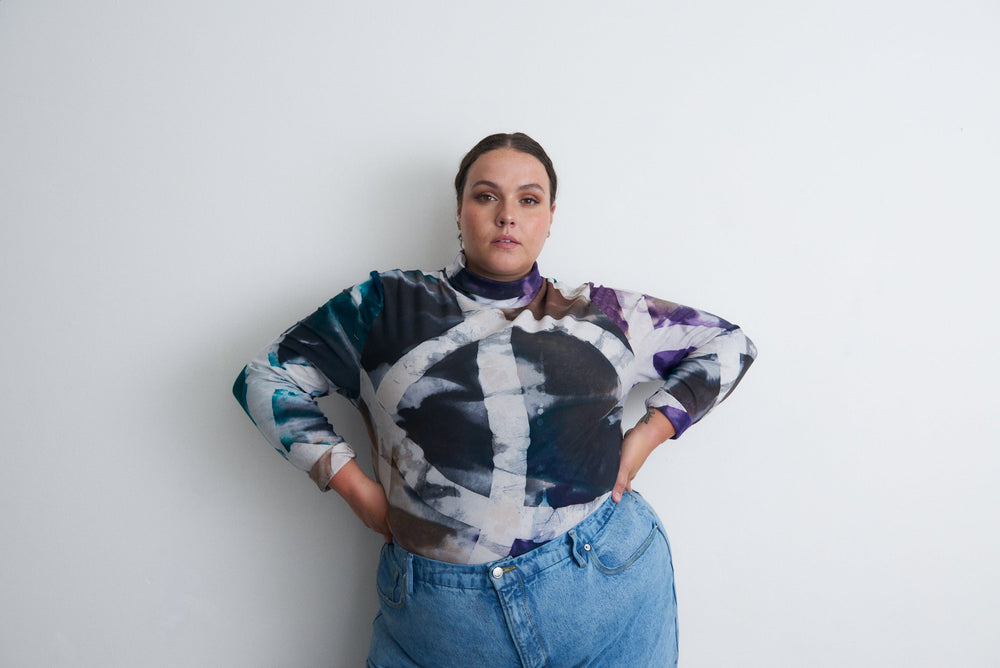 Person in the Stricta Turtleneck in Psychedelic Mangrove and high-waisted jeans, exuding confidence against a white backdrop.