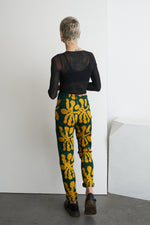 Back view of model in Vitta Trousers with sheer black top, highlighting the bold green and yellow floral print and fit.