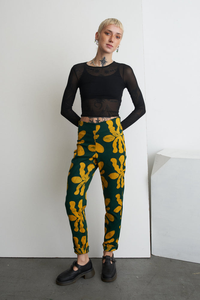 Model in Vitta Trousers stands against white corner, black see-through top, showcasing print and fit.