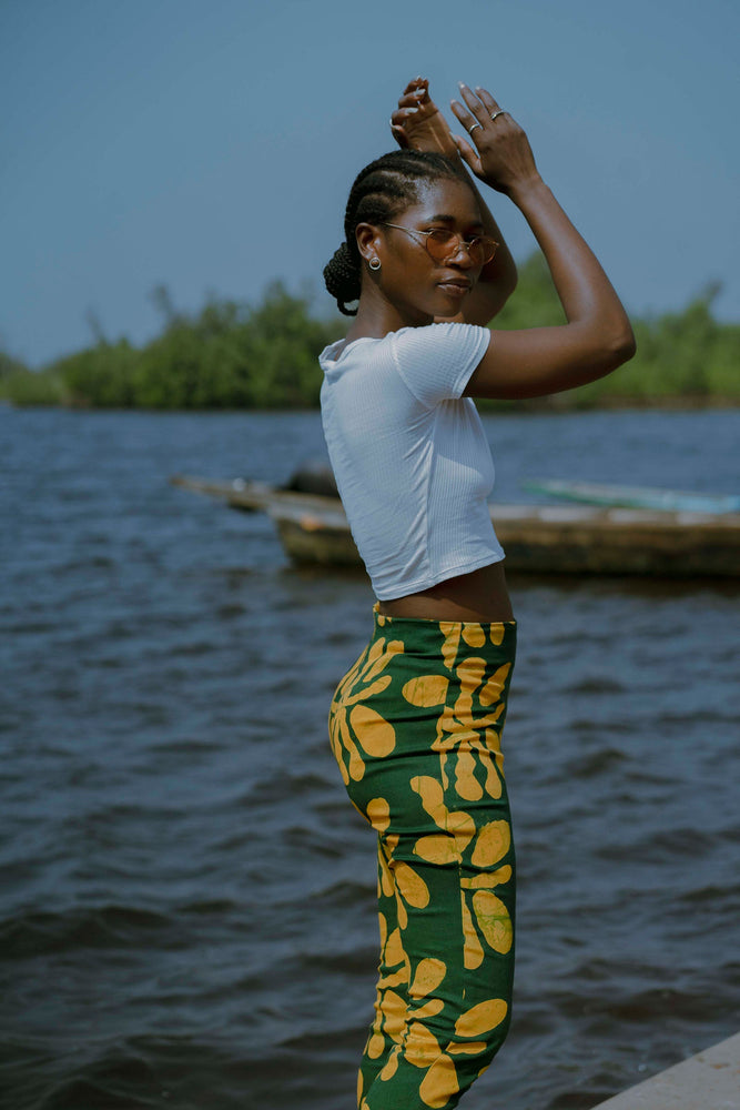 Model in Vitta Trousers stands by water, back turned, with hand on forehead, showcasing the high-waist fit and leaf print.