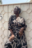 Fashionable woman in a hand-batiked print rayon wrap dress standing against a wall outdoors.