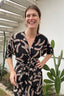 A stylish woman in a black and tan wrap dress posing confidently in front of a tall cactus.