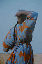 Back view of the Bating Dress in All Ideas print, striking a relaxed pose against a soft, overcast sky.
