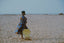 Person in All Ideas print Bating Dress gazes at ocean, standing on sandy beach with clear sky and beach chair.