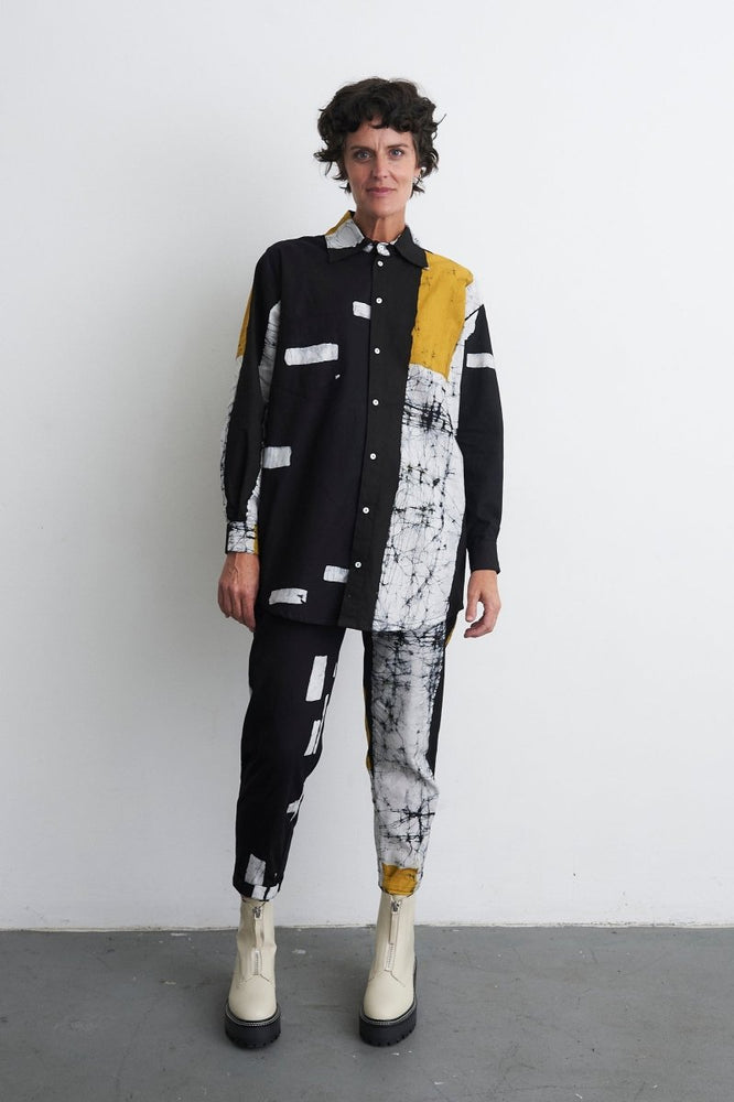 Eclectic Bula Shirt in black/white with yellow accent, paired with Kpong Trousers and beige boots, against a white wall.