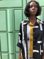 Model in Bula Shirt in Cut & Paste black/white/yellow print standing against a textured green wall. 