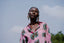 Woman wearing pink Bula Shirt with batik print resembling avocados, large hoop earrings, clear sky background.