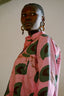 Side view of woman wearing pink Bula Shirt in Tunnel of Love with green abstract shapes, and large hoop earrings.