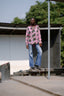 Woman standing on a raised platform in pink the Bula Shirt in Tunnel of Love an avocado-like print, blue flared jeans.