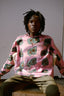 Person seated wearing a pink Bula Shirt with abstract green, black, and white patterns, and dark green pants.