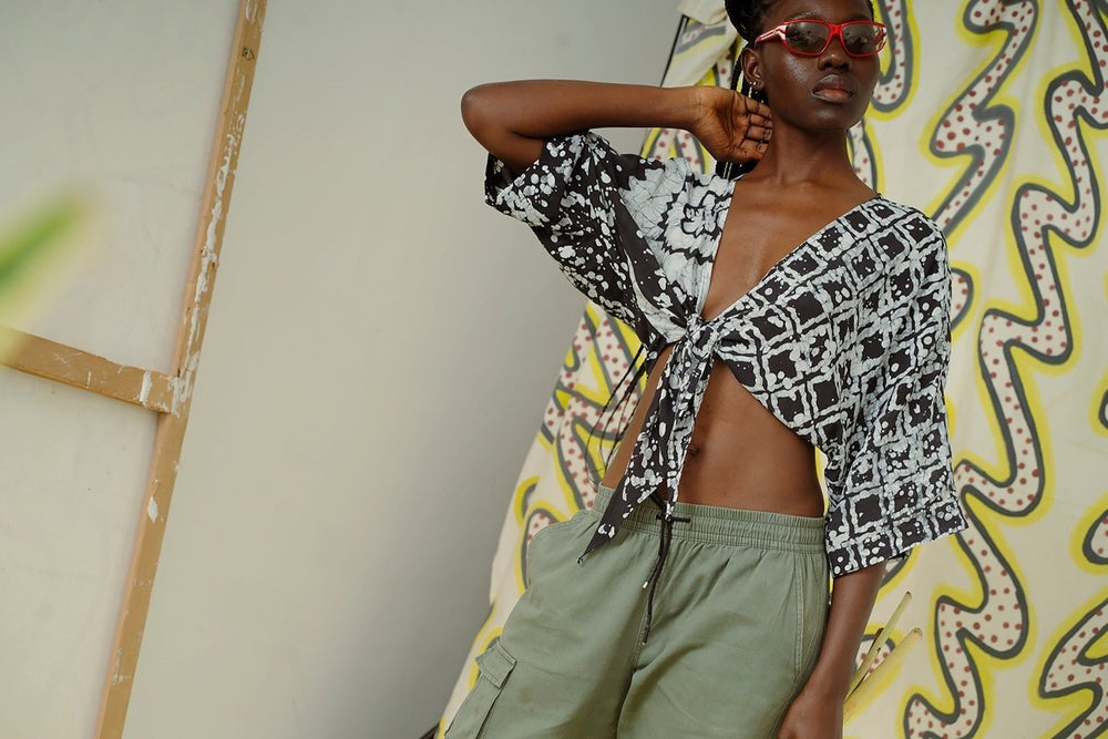 Osei-Duro Epo Tie Top in black & white floral grid 2 Party System print. Model wears colored sunglasses and olive trousers.