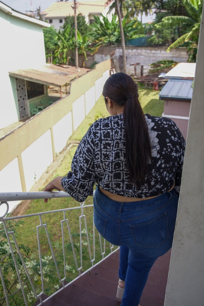 Model walks down stairs in Epo Tie Top in 2 Party System print, back view on balcony, overlooking buildings and greenery.