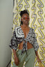 Epo Tie Top in 2 Party System print, front-tied, paired with olive pants, against patterned backdrop.