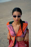 Model wears Epo Tie Top in Carmine print with sunglasses, sitting on the beach.