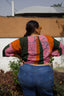 Epo Tie Top in Carmine print, captured from behind, paired with blue jeans, against a white building and greenery.