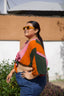 Outdoor shot of Epo Tie Top in vibrant Carmine print, paired with blue jeans, against a backdrop of white wall and greenery.