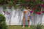 Person in Helia Dress with blue and orange print, standing by flowering plants on a white wall.