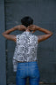 Back view of person in Index Vest with Long Division print and blue jeans, hands on back of head, against a dark background.