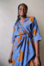 Elegant Letsa wrap dress with batwing sleeves, deep V neckline, and abstract orange flower print on sky blue background.