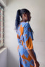 Back view of Letsa dress highlighting tie detail, side slits, and orange pattern on blue, worn by a person with curly locks.