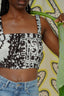 Summer crop Lupi Top in 2 Party System print, person holding green leaf, blue jeans, pale yellow patterned background.