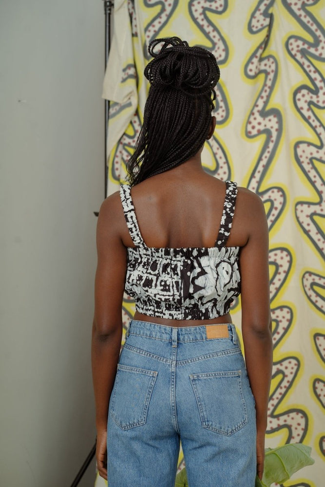 Rear view of Lupi Top in 2 Party System print, paired with high-waisted jeans against yellow patterned wall.
