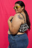 Model in Lupi Top in 2 Party System, a black & white split print, wearing sunglasses and blue jeans against pink backdrop.