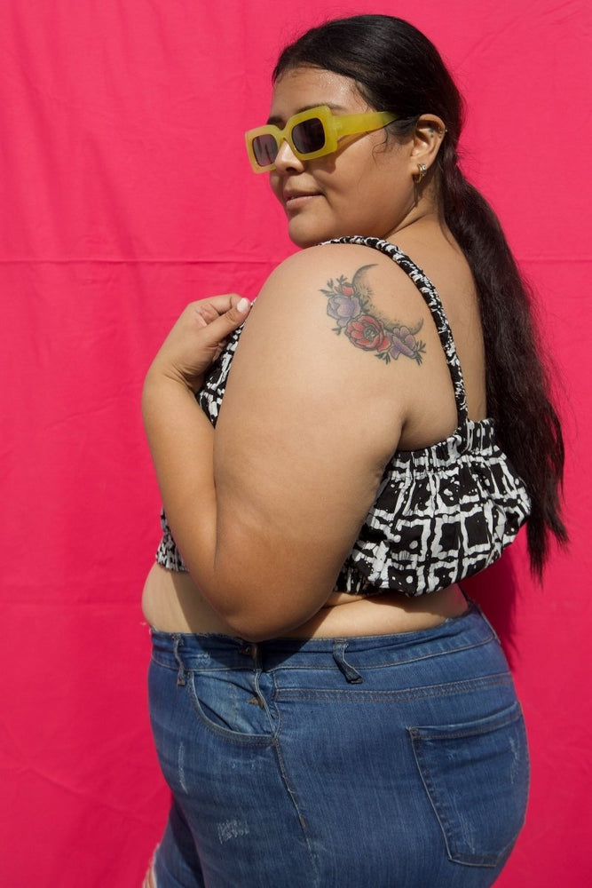 Model in Lupi Top in 2 Party System, a black & white split print, wearing sunglasses and blue jeans against pink backdrop.