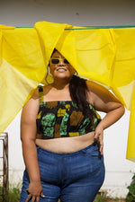 Model wears the Lupi Top in Pistacia outdoors with yellow fabric on a line above head. Paired with sunglasses and blue jeans.