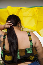 Back view of Lupi Top in Pistacia with yellow fabric in the background, tattoo on right arm, outdoor setting.