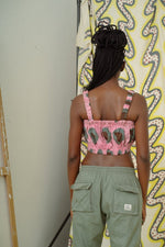 Rear view of Lupi Top in Tunnel of Love print with green oval patterns, paired with green pants, against wavy yellow wall.