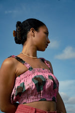 Side profile of Lupi Top in pink and green shapes Tunnel of Love print, against a cloudy blue sky.