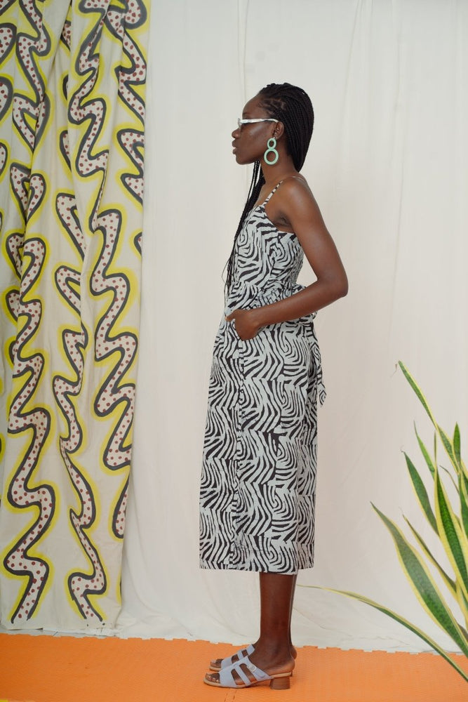Mafalda Jumpsuit with abstract black & white print, styled with sandals, against a green and yellow serpent curtain.