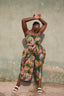 Dynamic Mafalda Jumpsuit, Waters print, green with pink/yellow patterns, white sandals, textured wall backdrop.