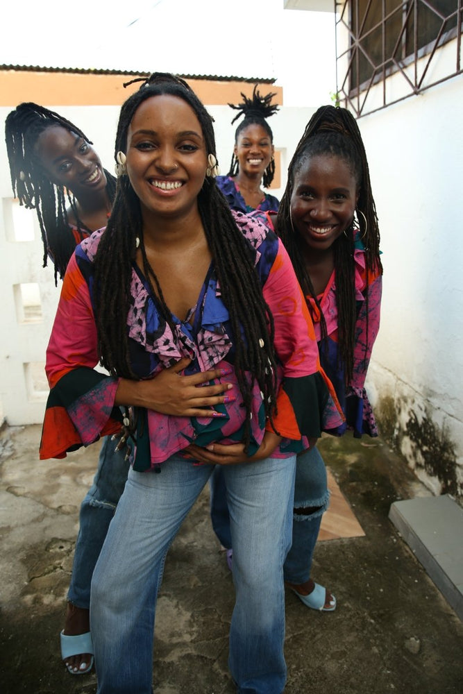 Playful style with Pastiche Clo’s blue and pink patterned shirt and denim, in an outdoor setting near a white building.